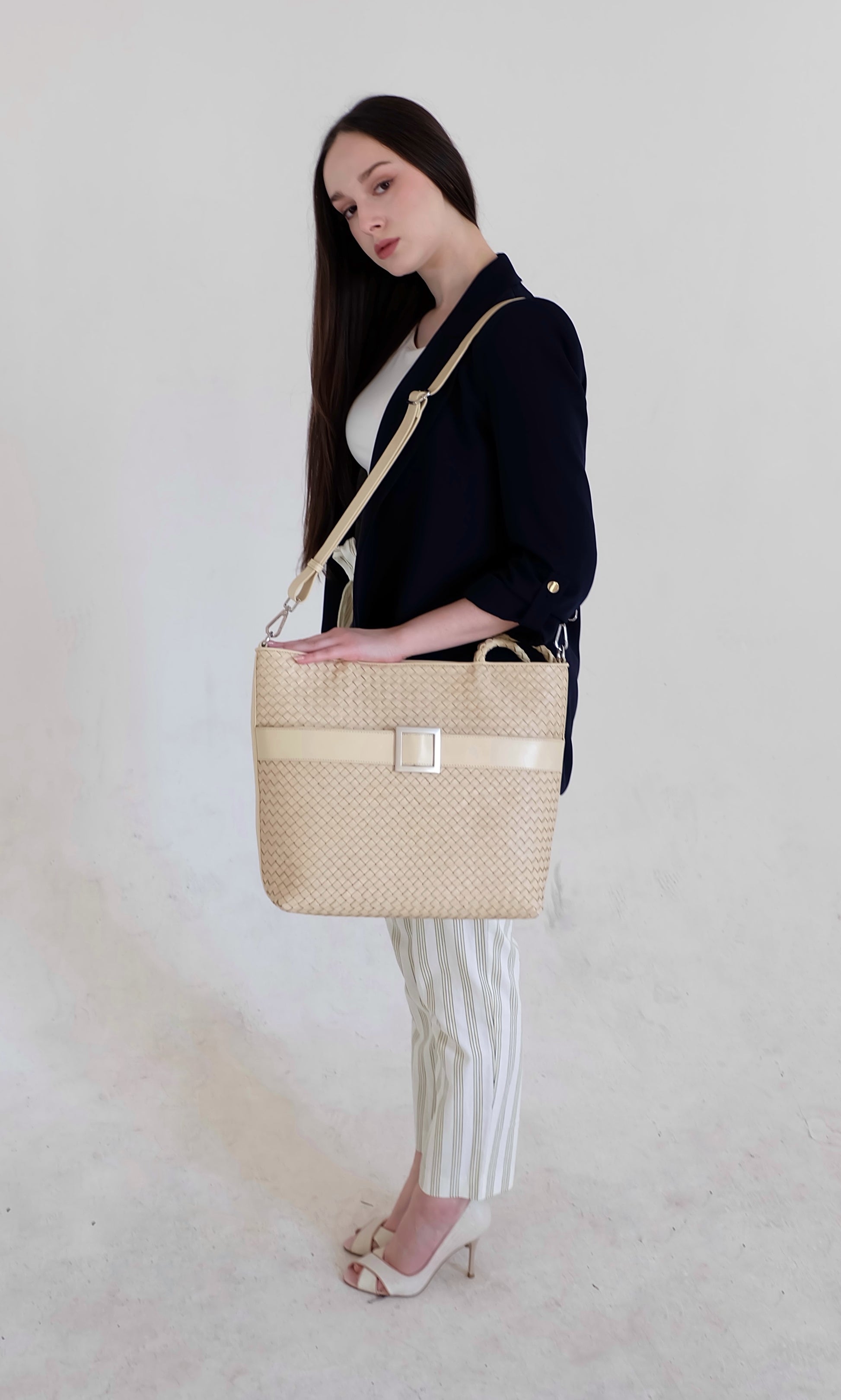 Beautiful, strong, independent, empowered and chic woman wearing a sustainable Italian leather designer handbag, medium tote and crossbody in cream. Handbag with accent buckle that is a functional work of art.