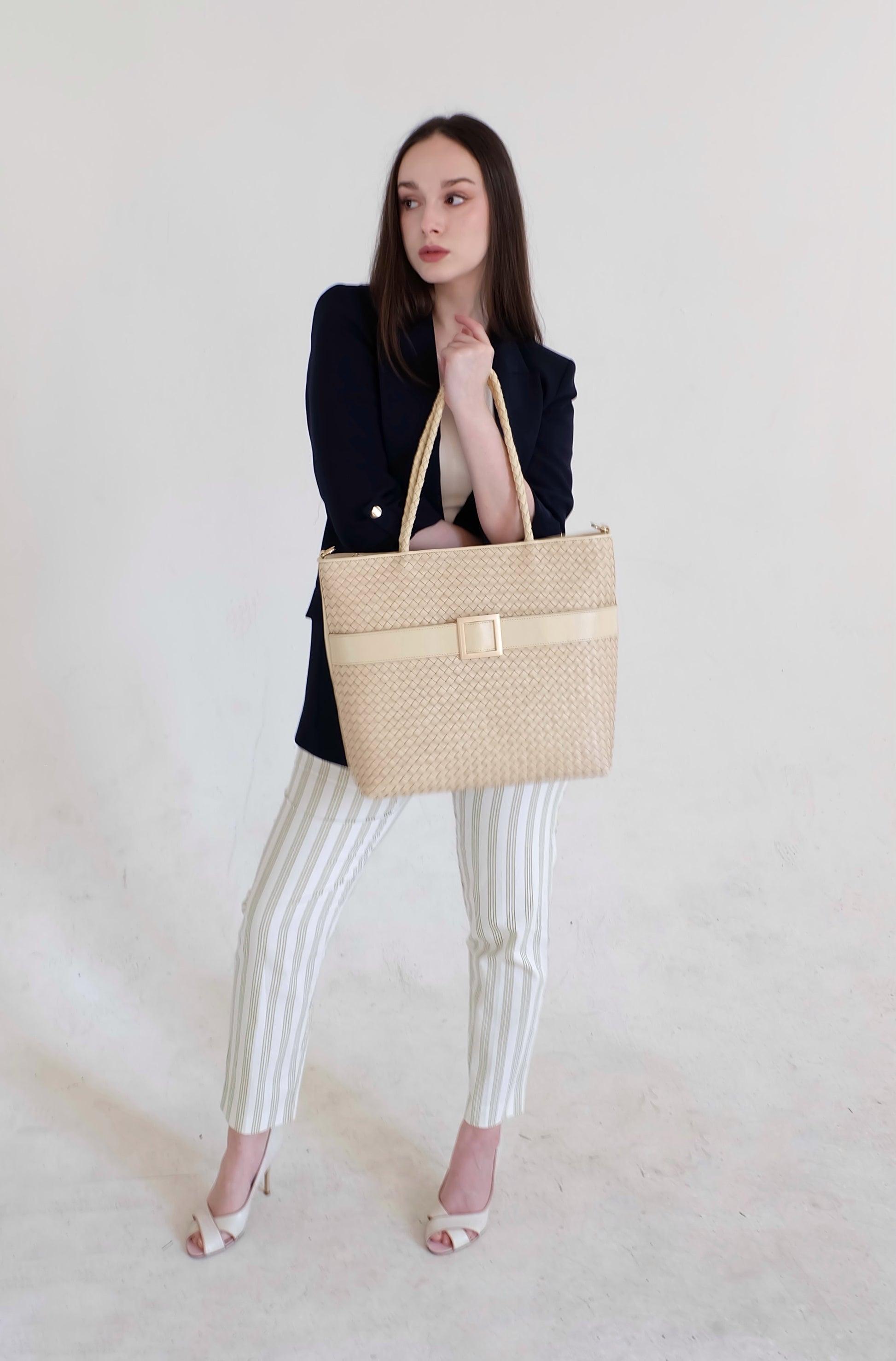 Beautiful, strong, independent, empowered and chic woman wearing a sustainable Italian leather designer handbag, medium tote and crossbody in cream. Handbag with accent buckle that is a functional work of art.