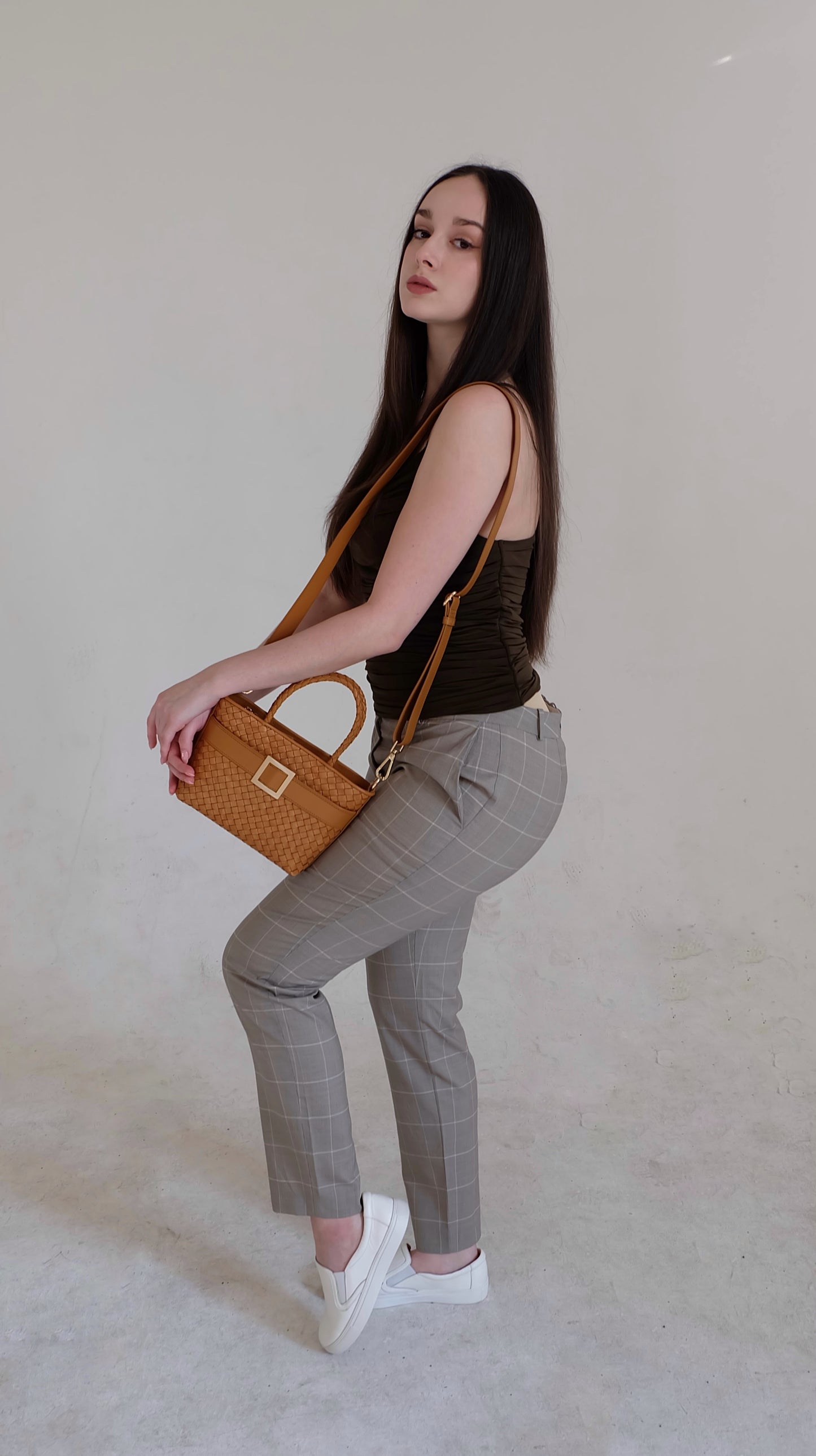 Beautiful, strong, independent, empowered and chic woman wearing a sustainable Italian leather designer handbag, mini tote and crossbody in cognac brown. Handbag with accent buckle that is a functional work of art.