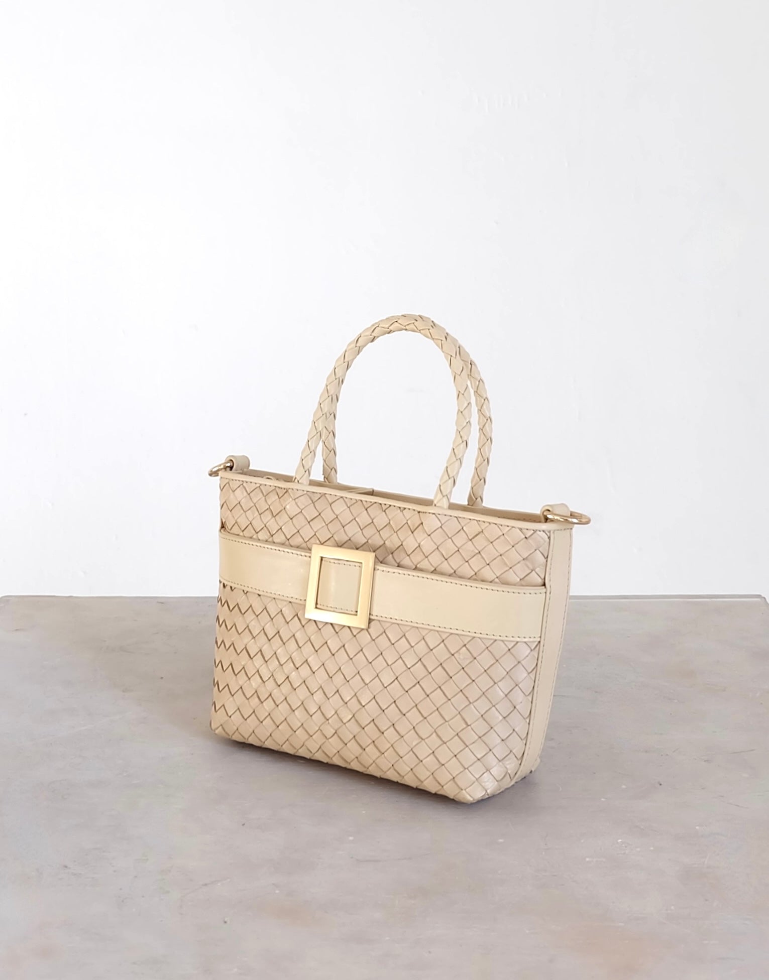 Sustainable Italian leather designer handbag in cream. Braided mini tote bag and crossbody in one, with accent buckle and front compartment.