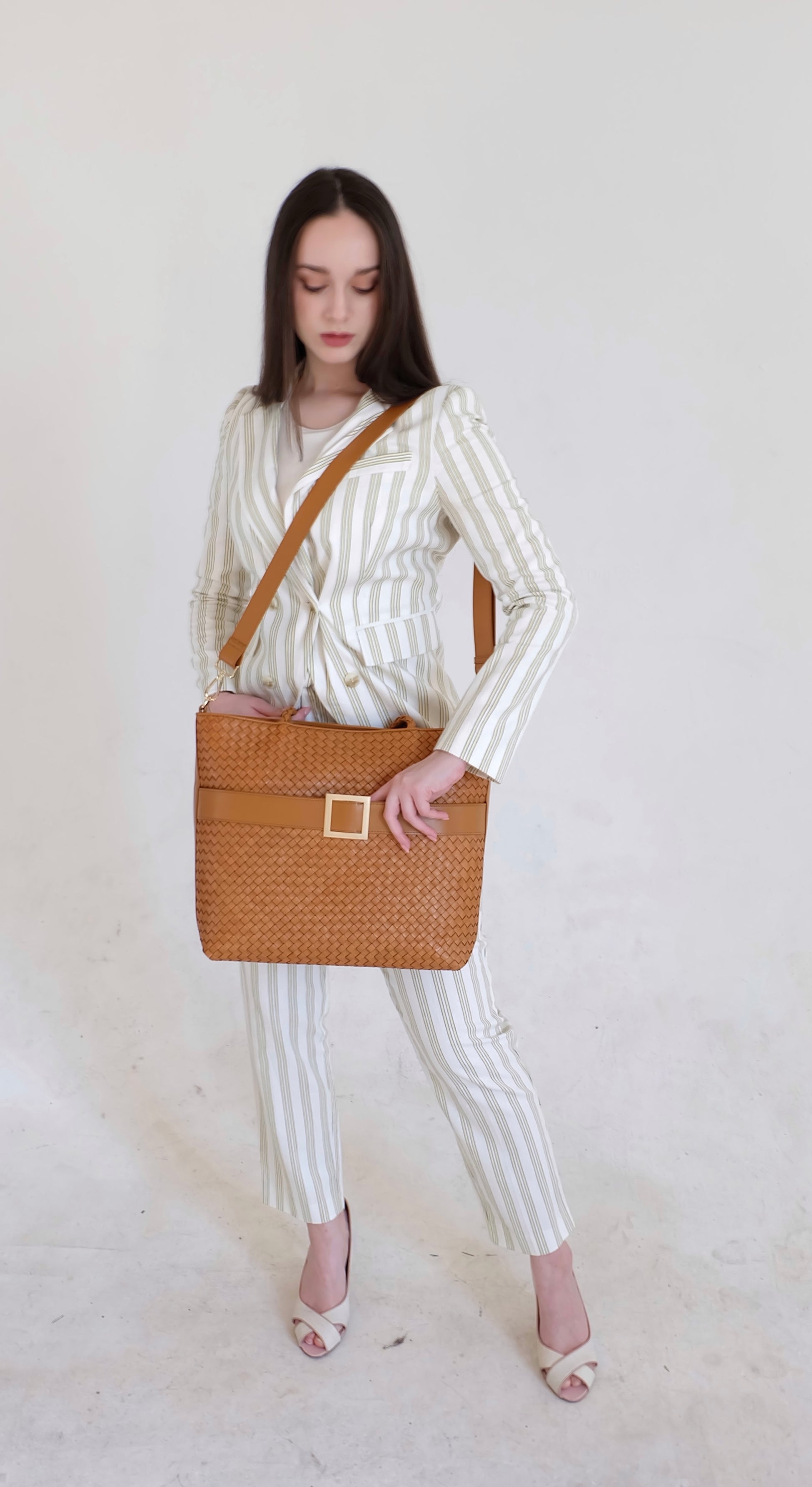 Beautiful, strong, independent, empowered and chic woman wearing a sustainable Italian leather designer handbag, medium tote and crossbody in cognac brown. Handbag with accent buckle that is a functional work of art.
