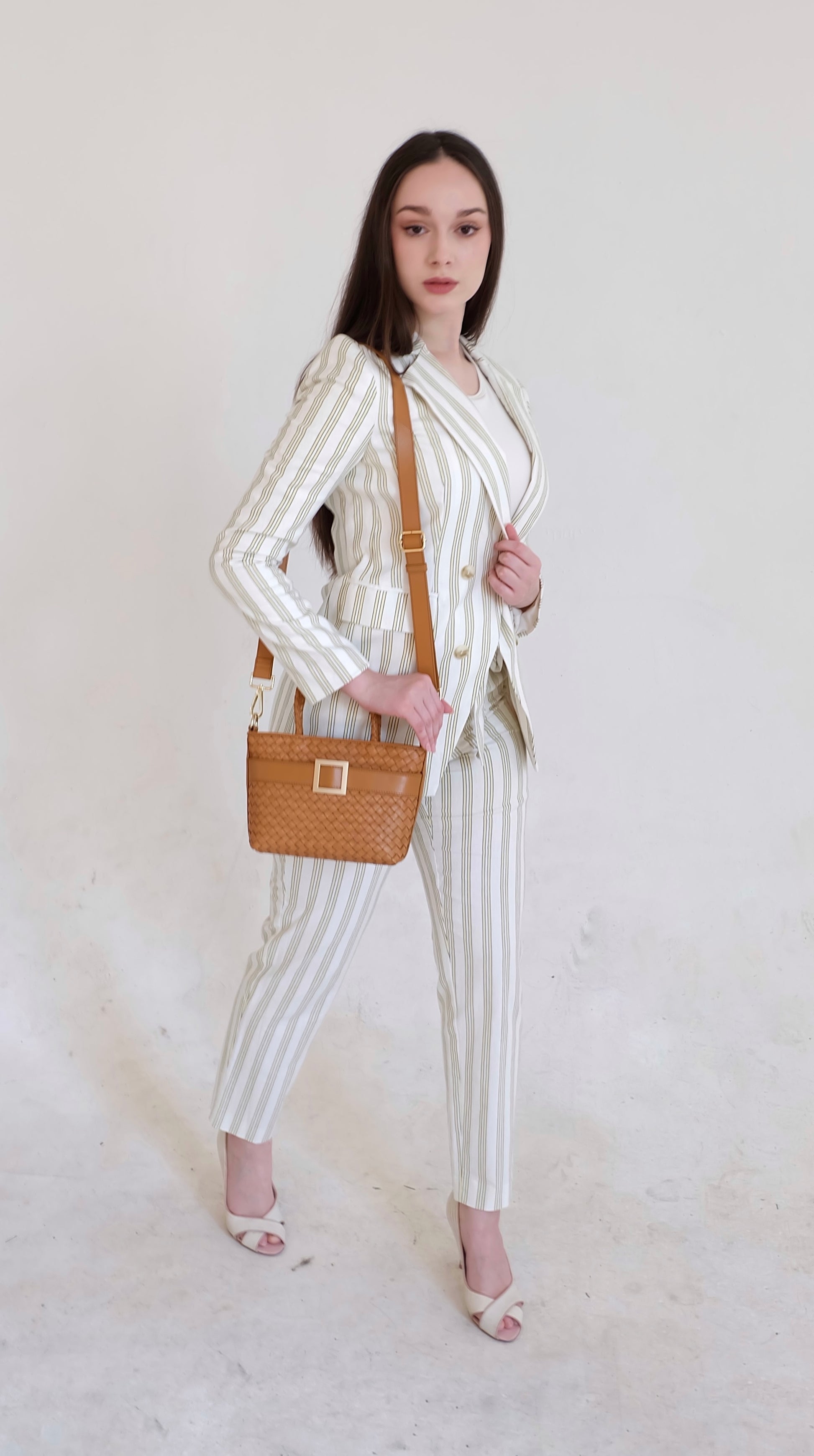 Beautiful, strong, independent, empowered and chic woman wearing a sustainable Italian leather designer handbag, mini tote and crossbody in cognac brown. Handbag with accent buckle that is a functional work of art.