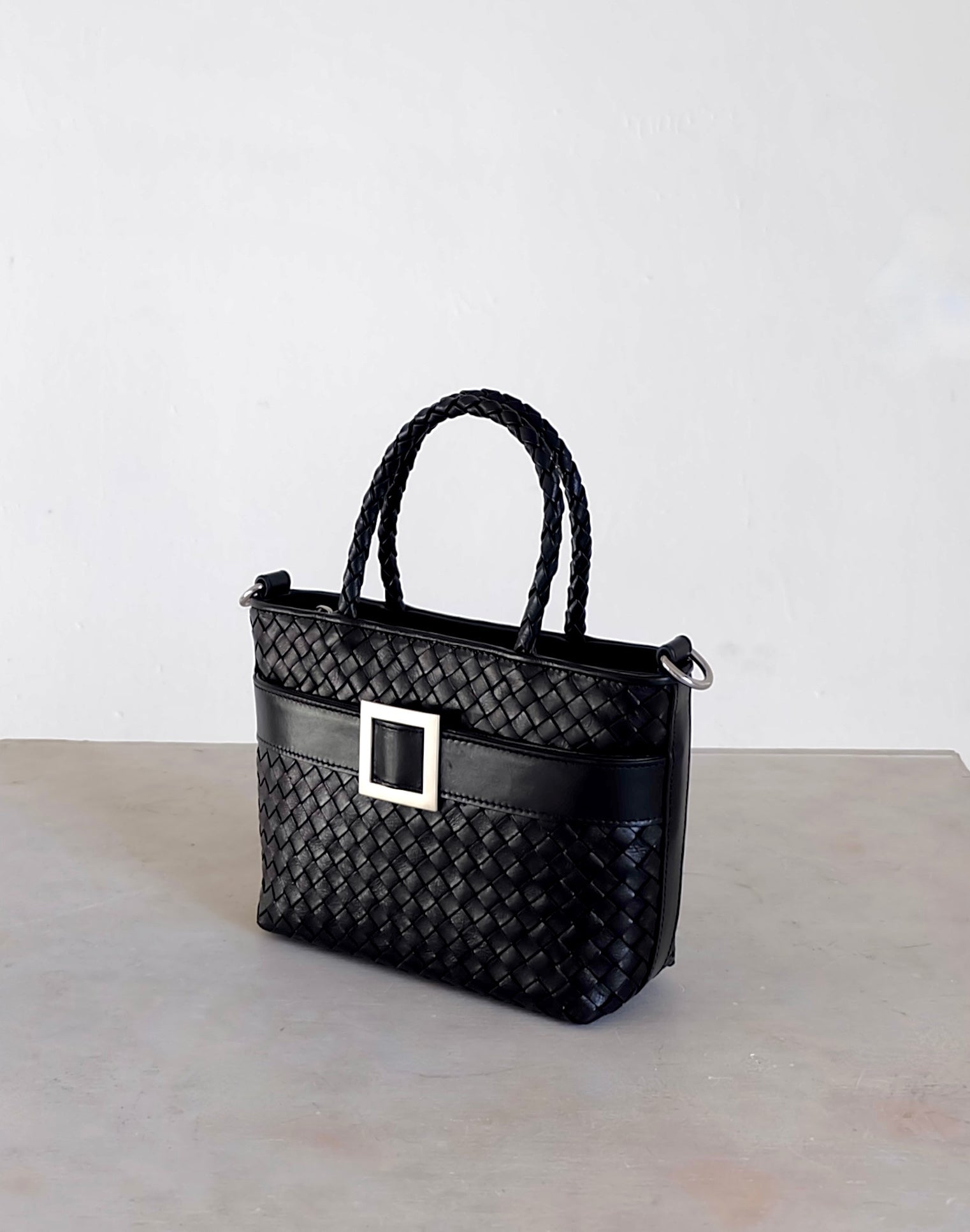 Sustainable Italian leather designer handbag in charcoal black. Braided mini tote bag and crossbody in one, with accent buckle and front compartment.