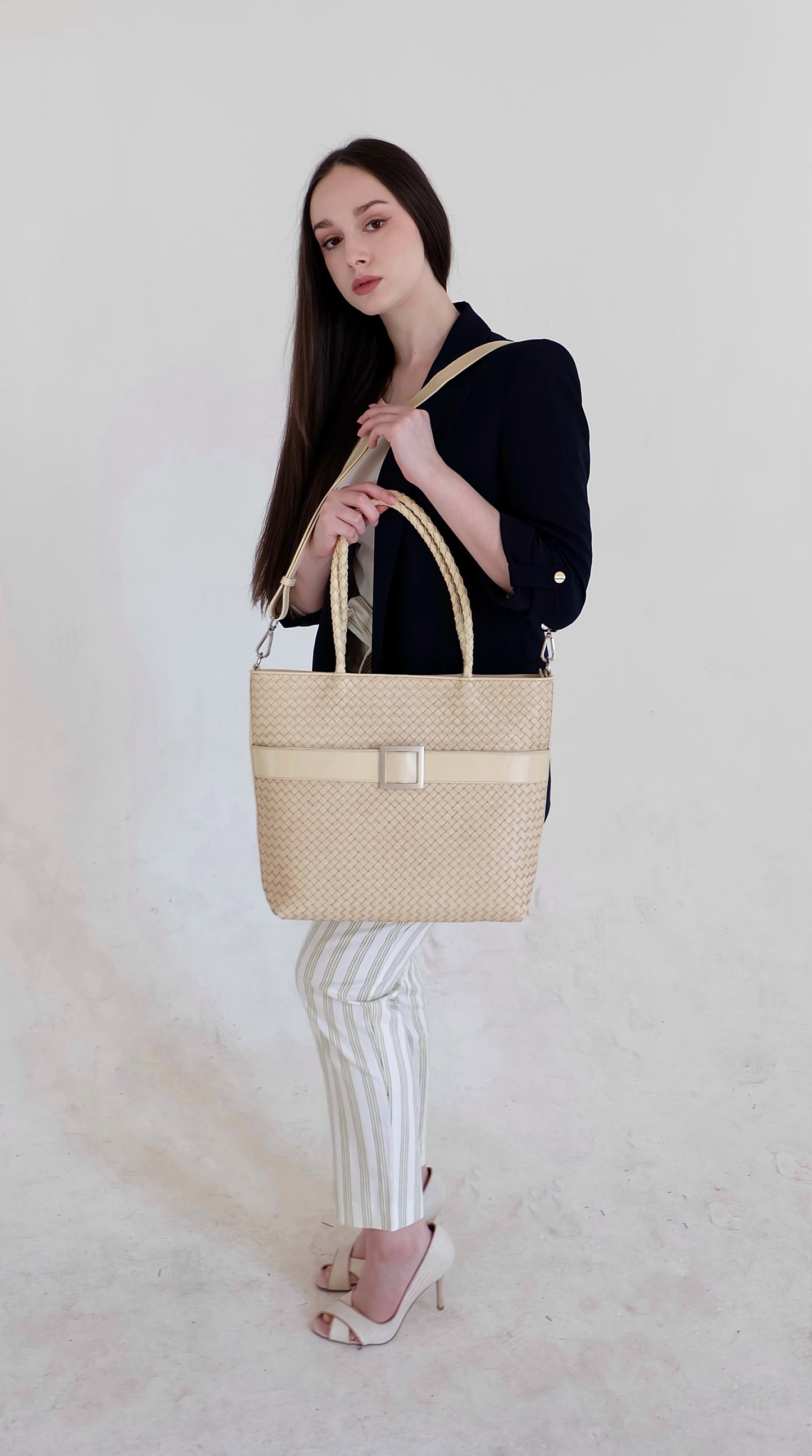 Beautiful, strong, independent, empowered and chic woman wearing a sustainable Italian leather designer handbag, medium tote and crossbody in cream. Handbag with accent buckle that is a functional work of art.