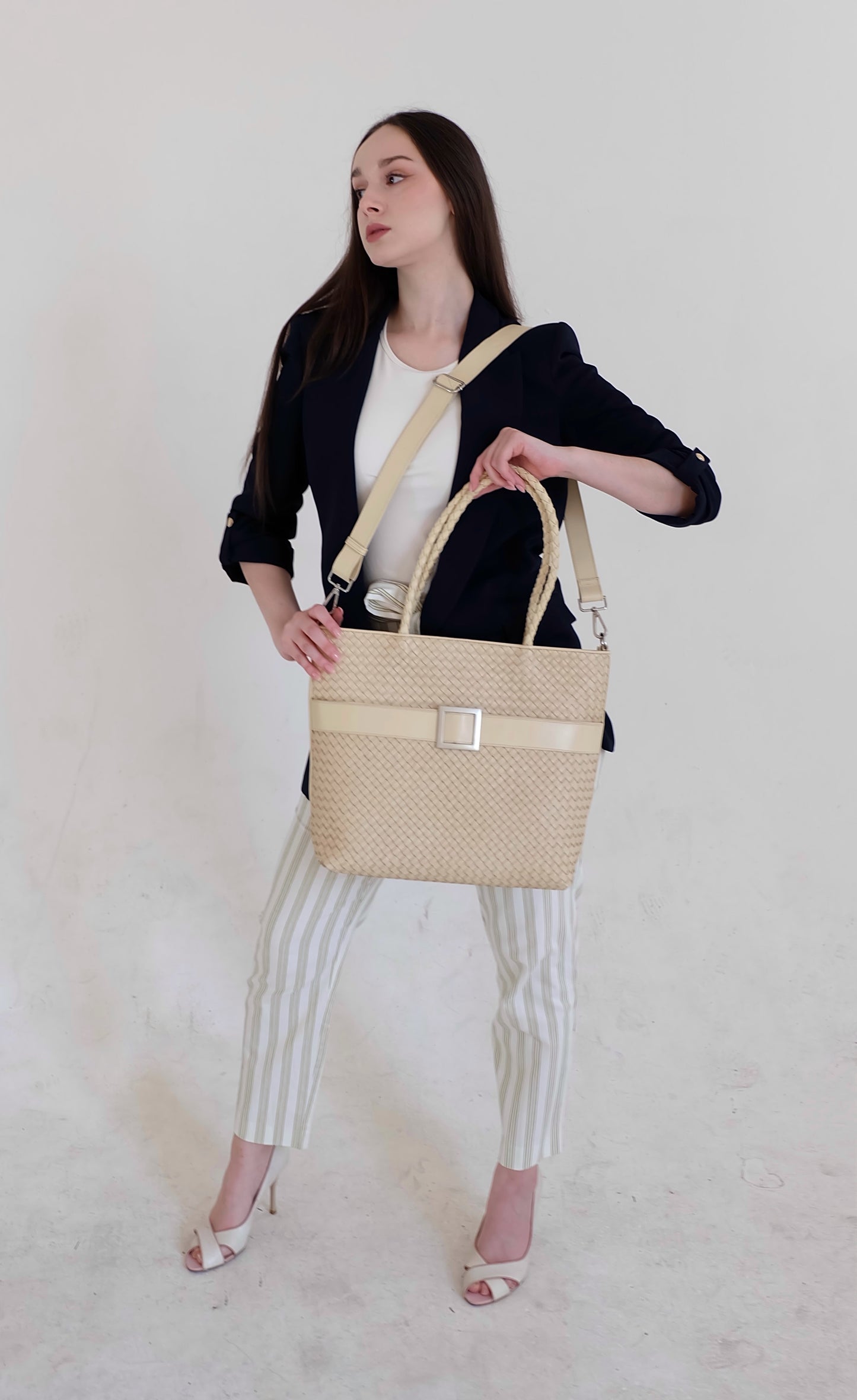 Beautiful, strong, independent, empowered and chic woman wearing a sustainable Italian leather designer handbag, medium tote and crossbody in cream. Handbag with accent buckle that is a functional work of art.