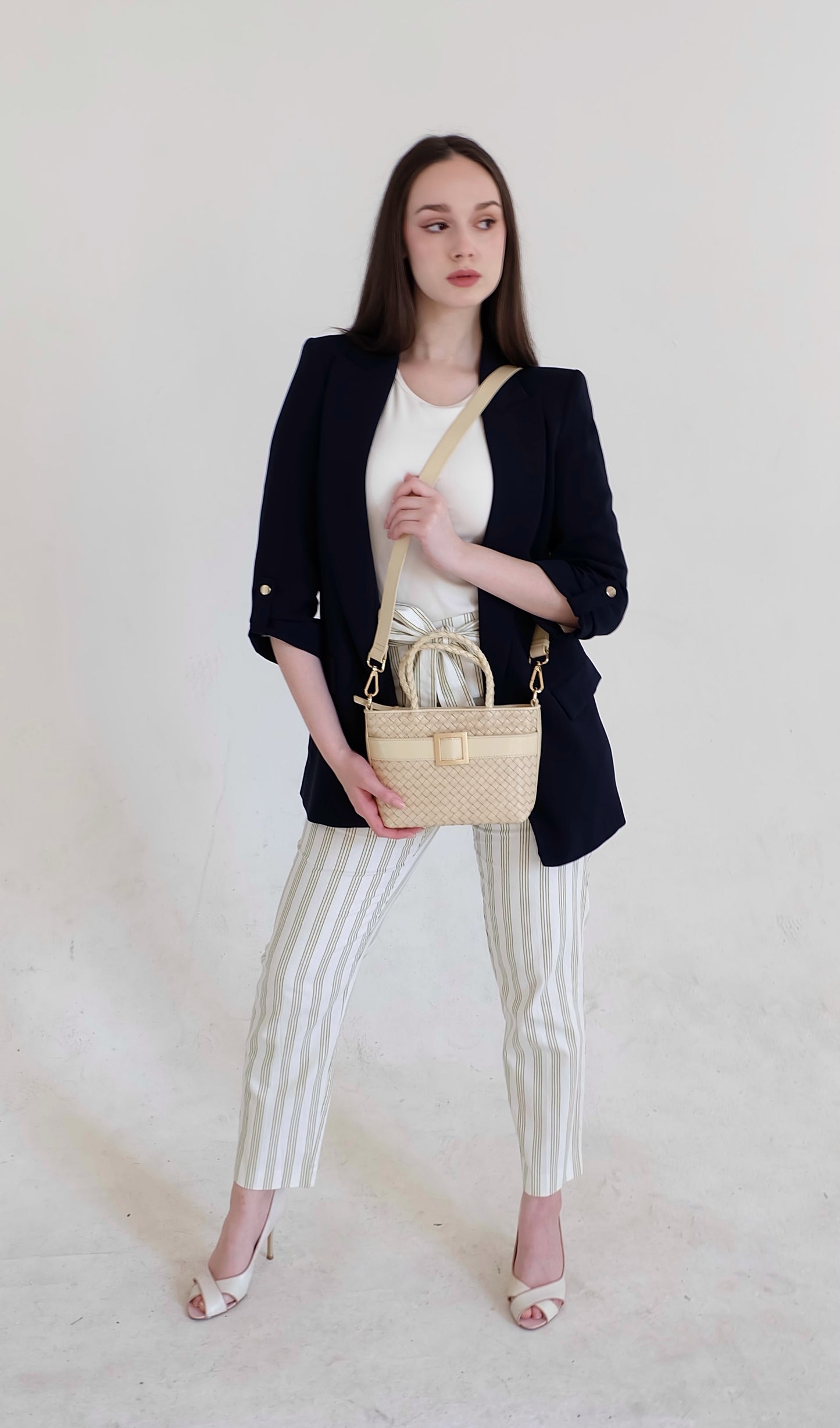 Beautiful, strong, independent, empowered and chic woman wearing a sustainable Italian leather designer handbag, mini tote and crossbody in cream. Handbag with accent buckle that is a functional work of art.