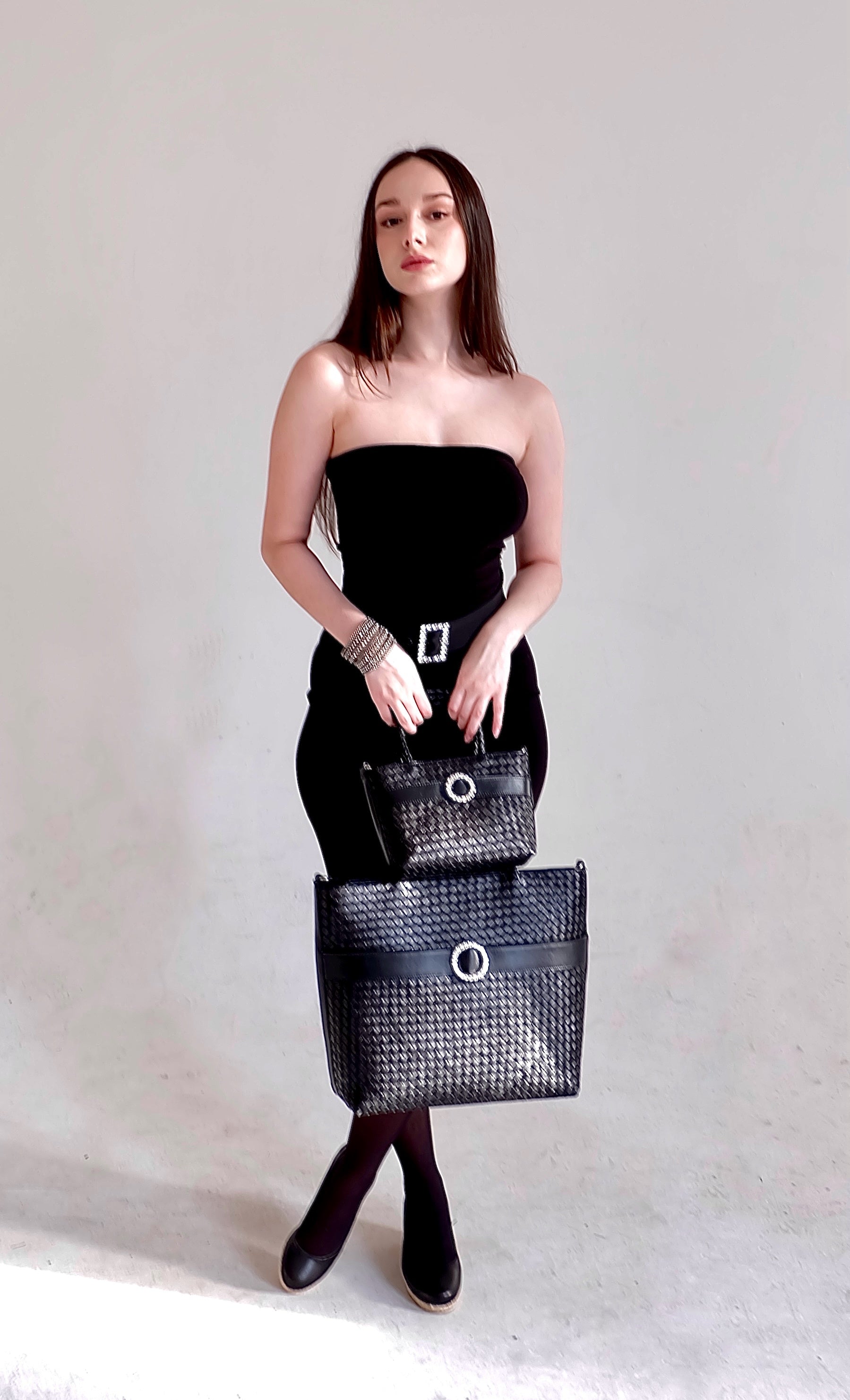 Beautiful, strong, independent, empowered and chic woman wearing a sustainable Italian leather designer handbag, mini and medium tote and crossbody in charcoal-black. Handbag with accent buckle that is a functional work of art.