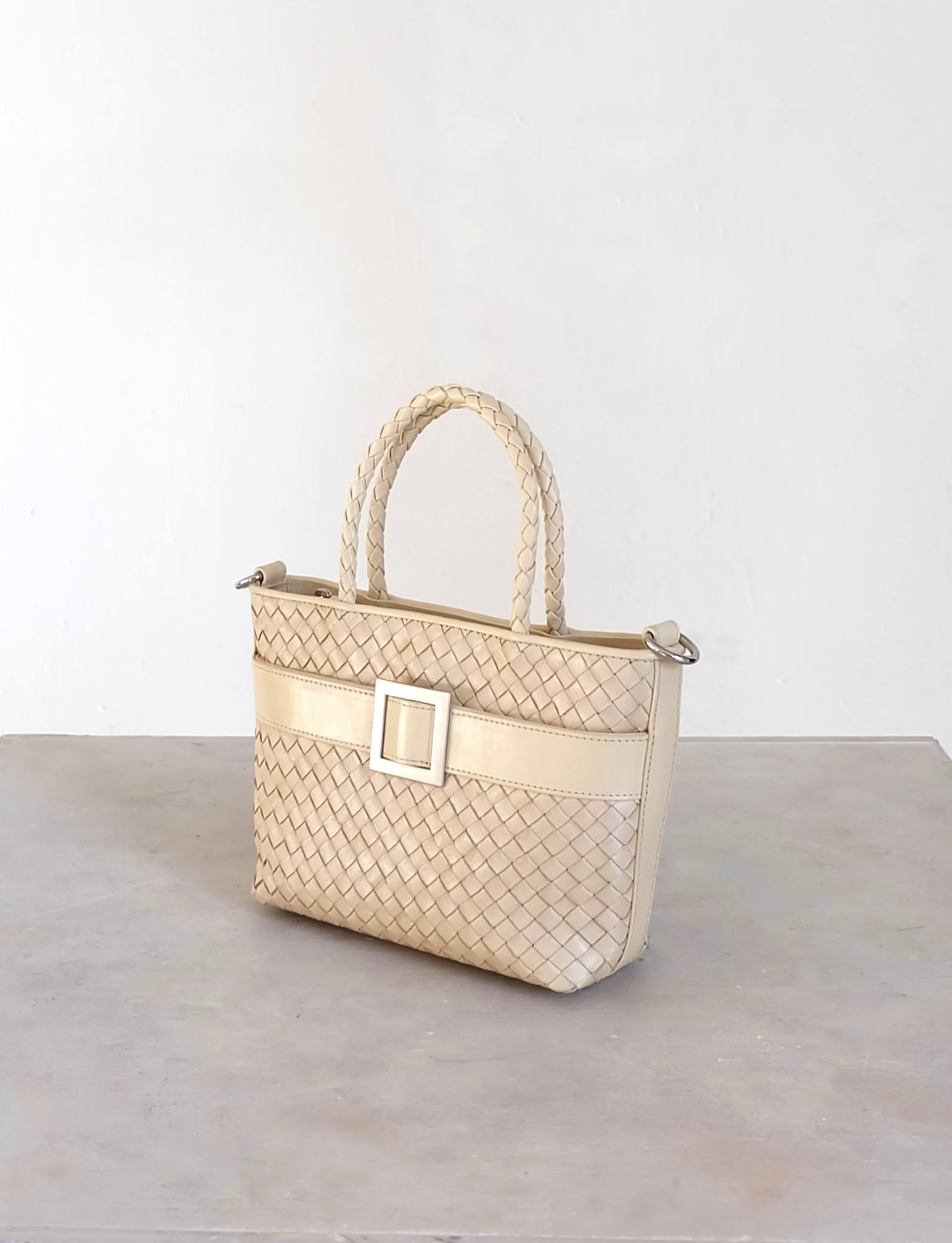 Sustainable Italian leather designer handbag in cream. Braided mini tote bag and crossbody in one, with accent buckle and front compartment.